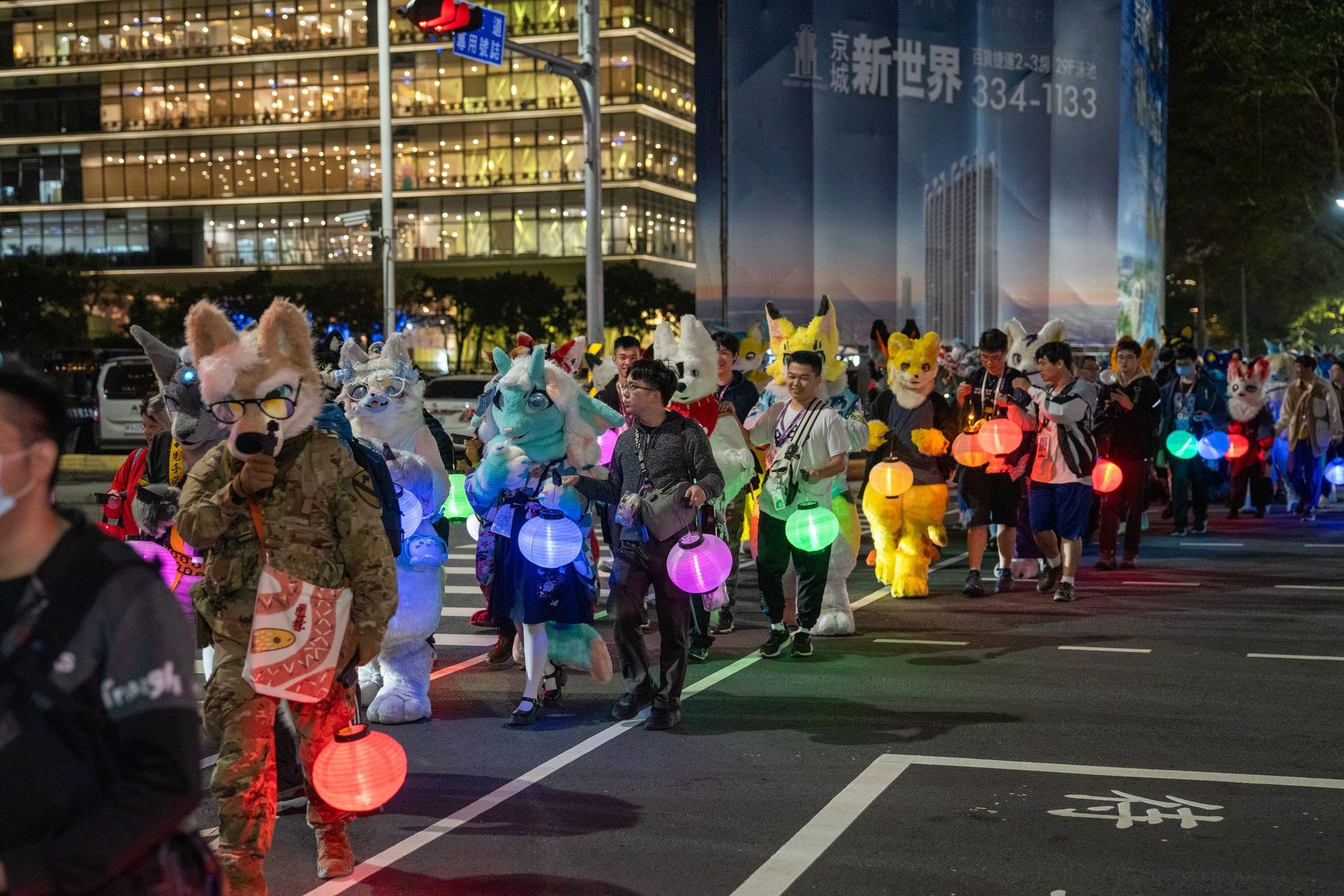 獸裝參加者手持繽紛發光燈籠列隊夜遊，街道兩側路燈與大樓燈火通明。