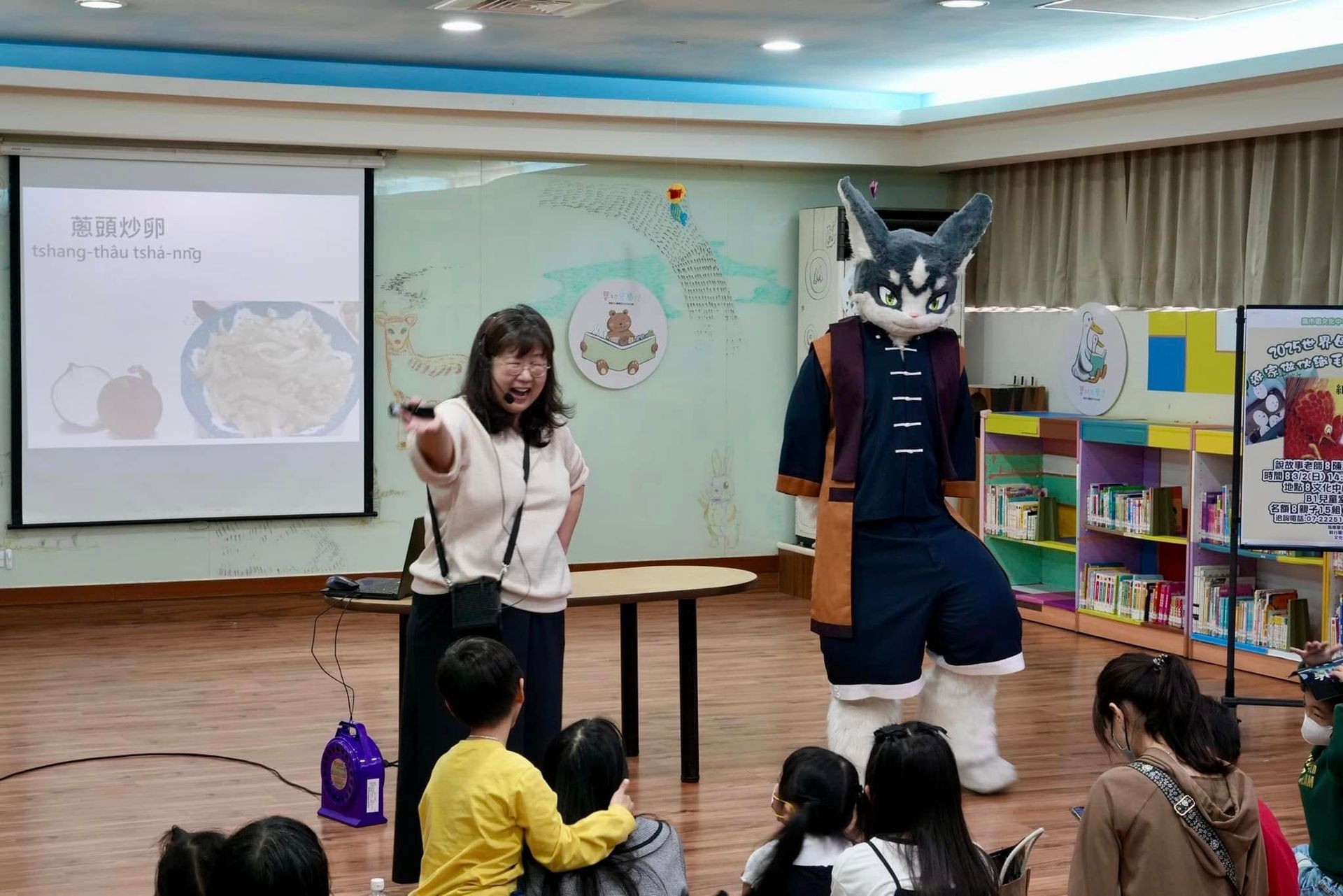 獸裝參加者在圖書館內陪同講者介紹台語詞彙「蔥頭炒卵」，兒童席地聆聽。