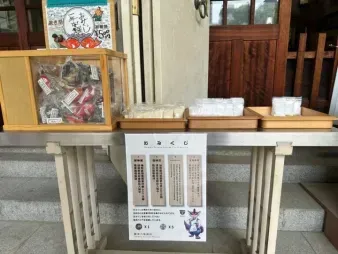 An omikuji (fortune slip) stand at a shrine, with stacks of paper fortunes and drawing boxes on a wooden table.