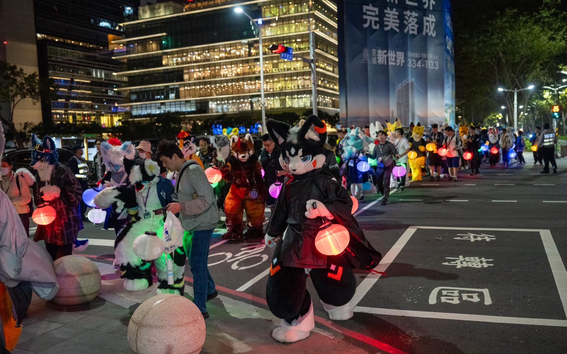 大批獸裝參加者在高雄市區街道上手持彩色發光燈籠夜間遊行，背景可見高樓與招牌燈光。