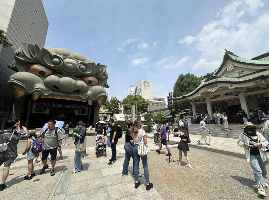 日本難波八阪神社廣場照片,可見巨大獅子造型裝置與神社建築,遊客往來其間