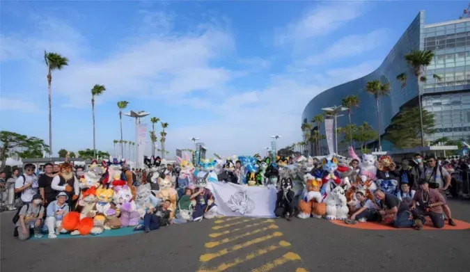 A large group of fursuiters lines up for a photo outside Dream Mall Plaza, with a hand-drawn team banner displayed in the center.