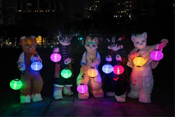 五位獸裝參加者夜間站在公園草地上合影,手持發光燈籠,背景為城市高樓燈火。