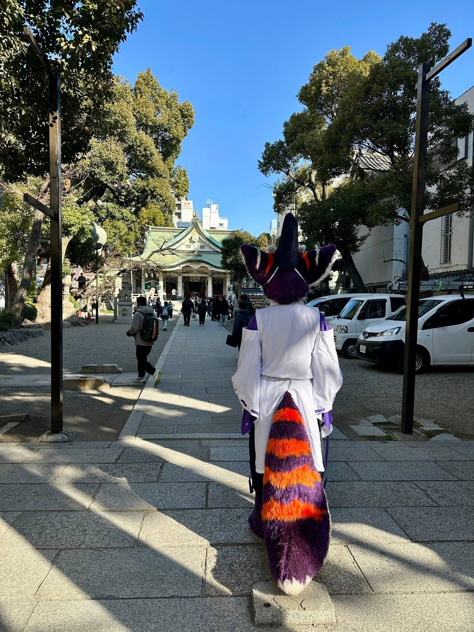 紫橙配色獸裝角色從背後望向神社本殿方向前行,路旁停有多輛白色小貨車