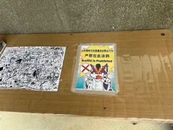 Printed "graffiti prohibited" signage: a black-and-white draft and the finished color version placed side by side on a cardboard box.