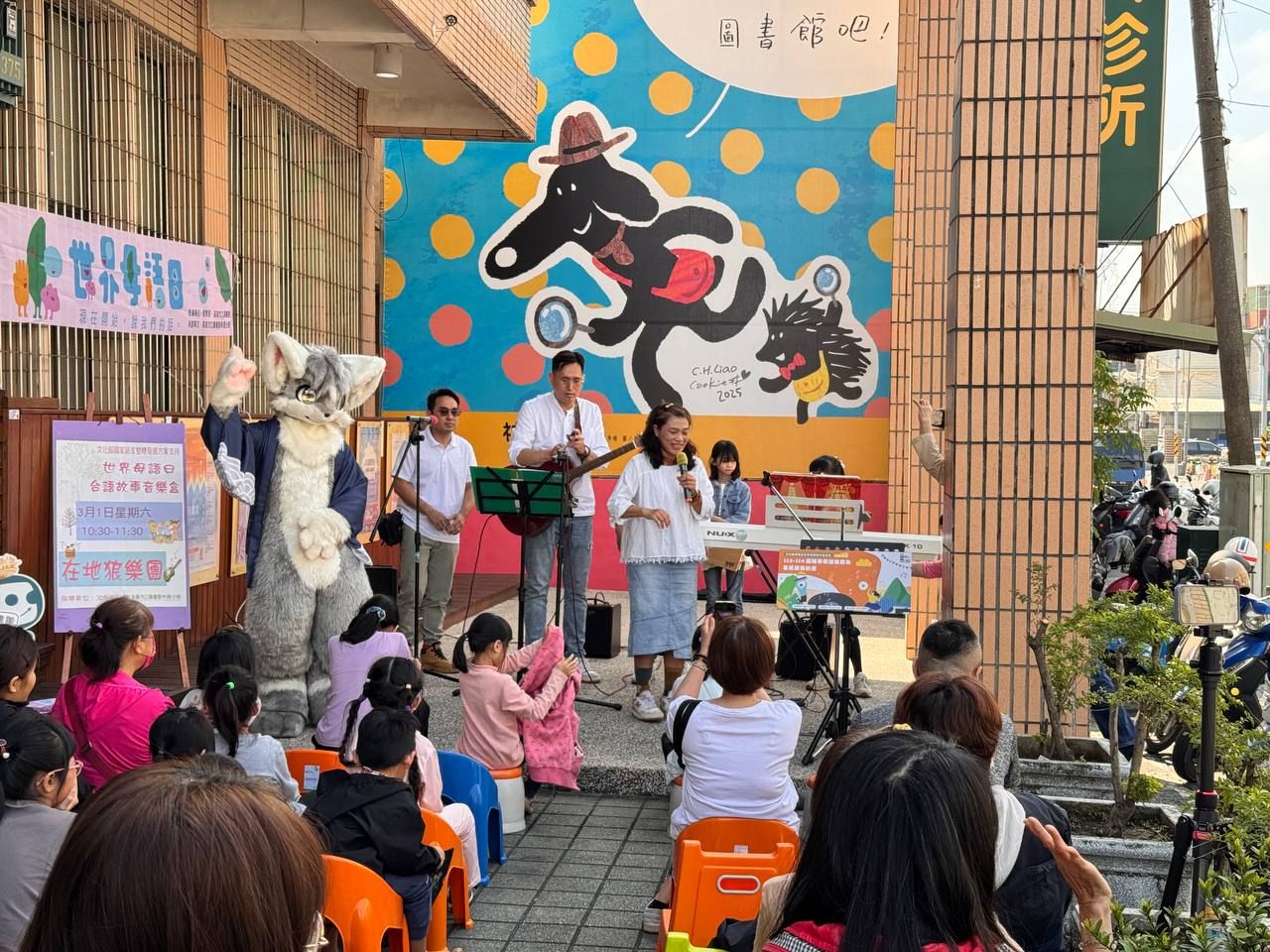 獸裝參加者在林園分館前街頭表演，樂團與主持人正演出台語故事音樂會，兒童席地觀賞。