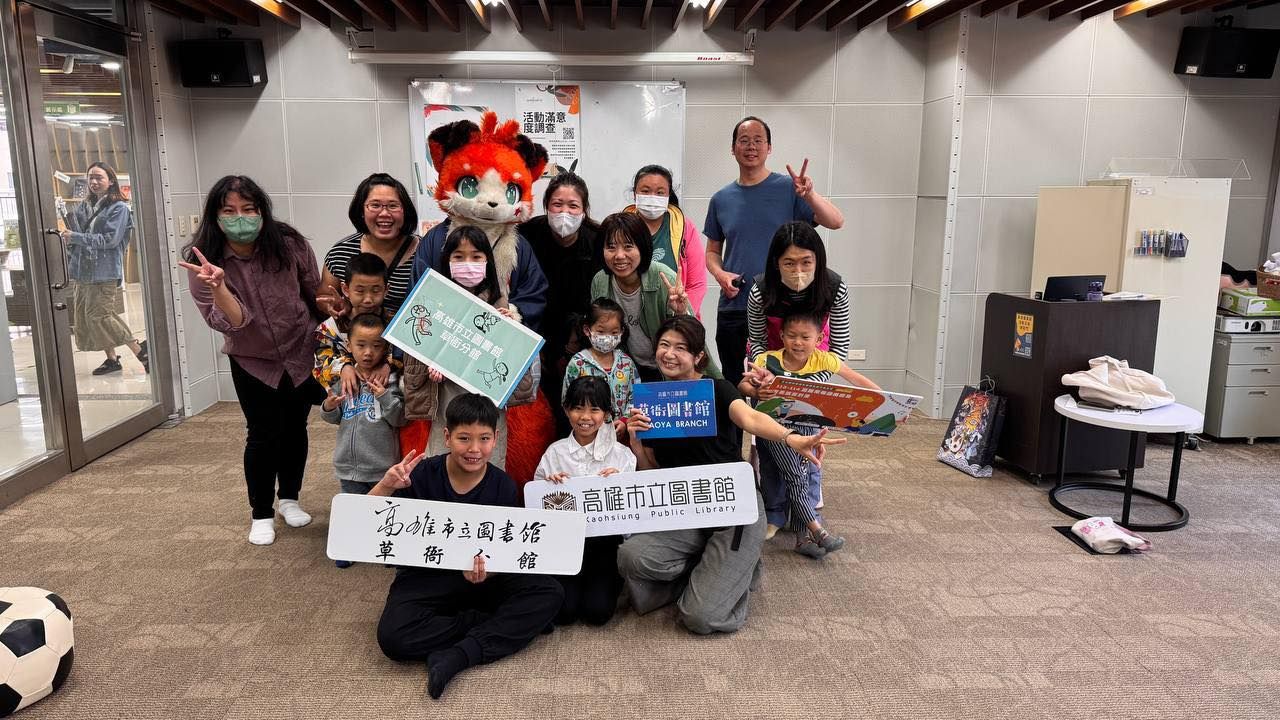 活動結束後大合照,橘色狐狸獸裝角色與參加的親子們一同比出勝利手勢,孩子們舉著「高雄市立圖書館草衙分館」看板。
